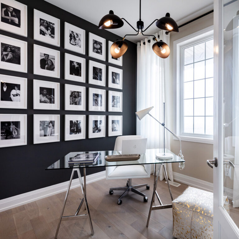 Home office with photo gallery on dark accent wall, glass and metal desk, and modern accents.